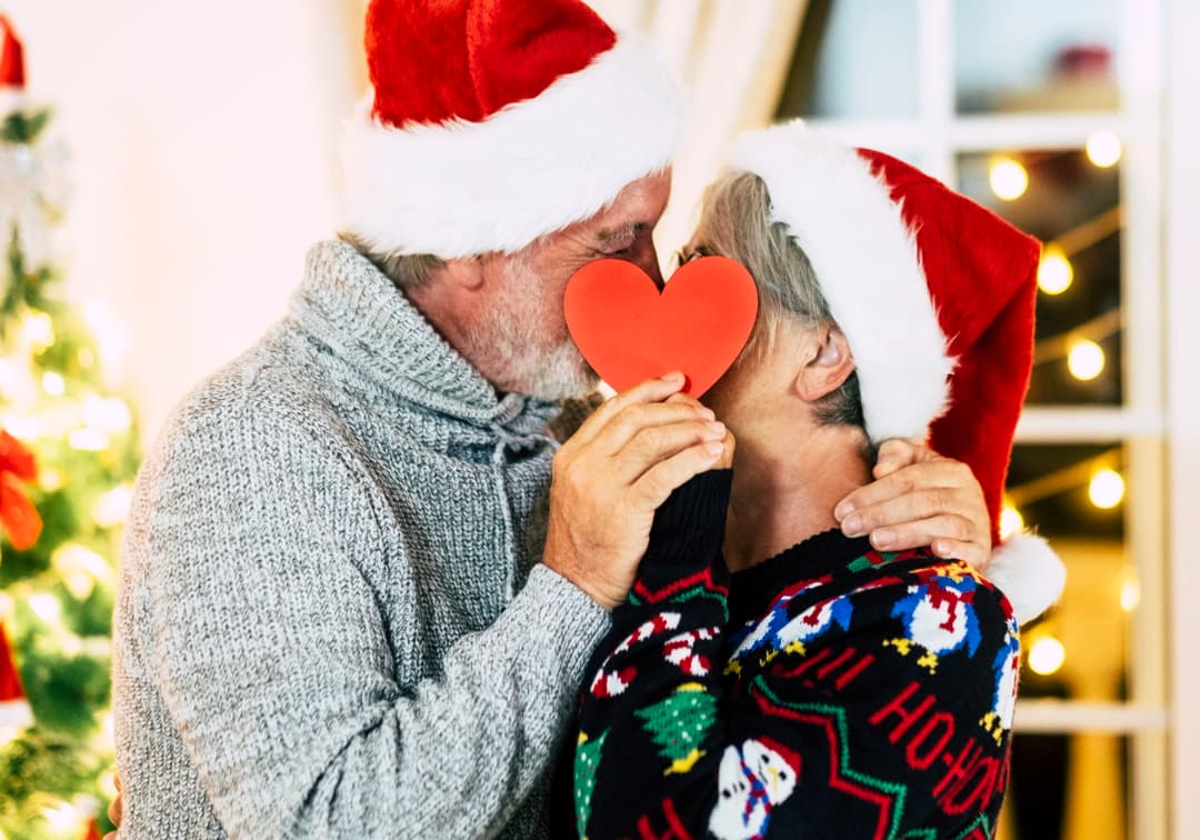 Couple in Santa hats sharing a kiss behind a paper heart
