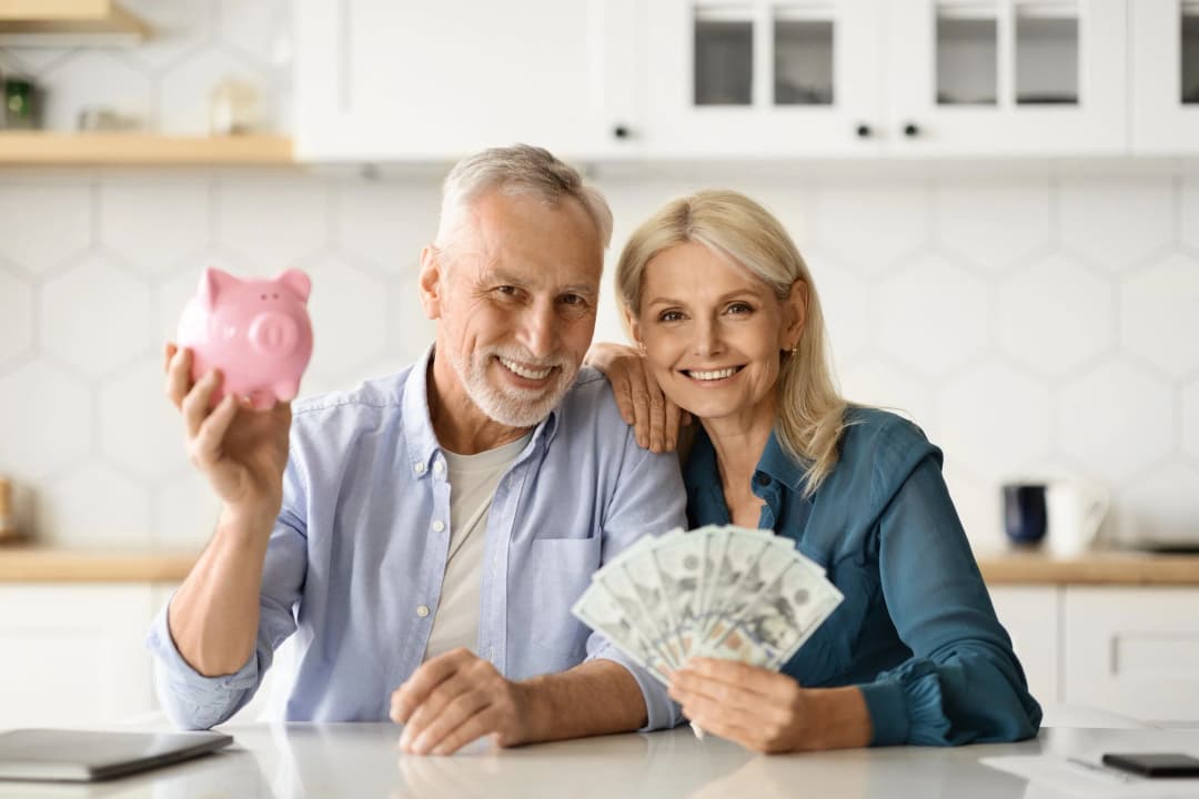 Couple at a kitchen counter holding a piggy bank and cash